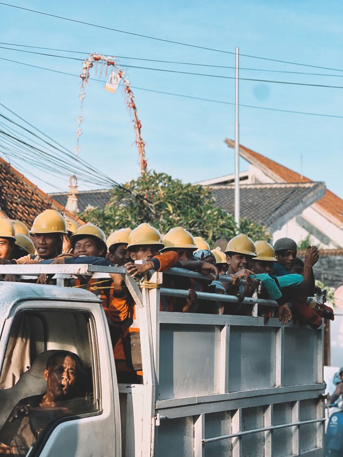 Workers in hard hats riding a truck through a bustling street in Ubud, Bali, Indonesia.
